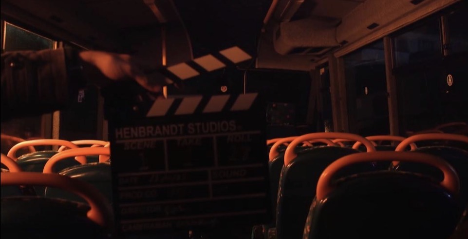 A clapperboard reading Henbrandt Studios held up inside a dimly lit coach
