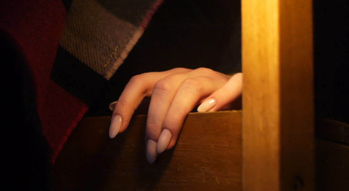 A hand resting on the back of a wooden chair in low amber light